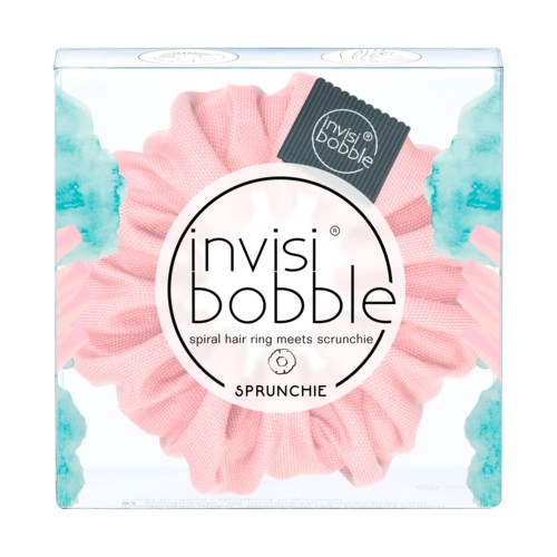 Ljus rosa scrunchie med svart etikett i genomskinlig box, kallad Invisibobble Sprunchie, för hårstyling.