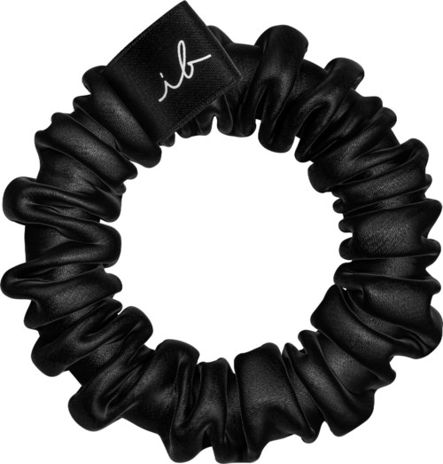 En svart scrunchie med en liten vit logotyp eller initialer. Den är gjord av glänsande tyg och ser mjuk ut.