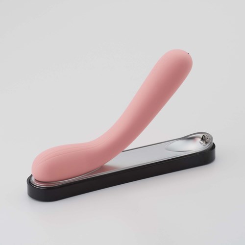 Et rosa, bøyd objekt på en svart og grå base, som ligner en massasjer eller lignende enhet.
