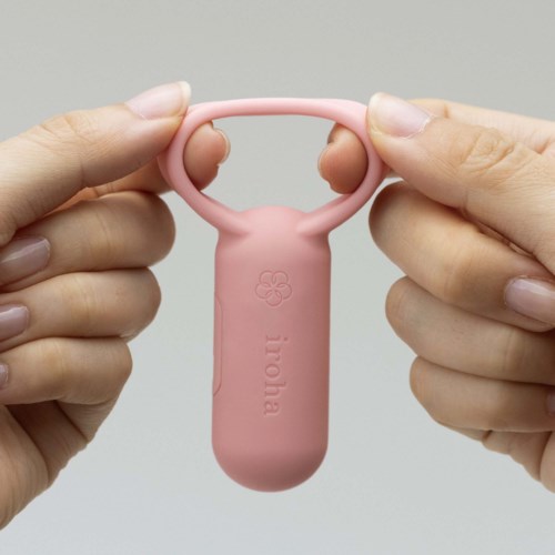 A person holds a small pink silicone tool with two finger holes and a flower design, labeled "ioma."