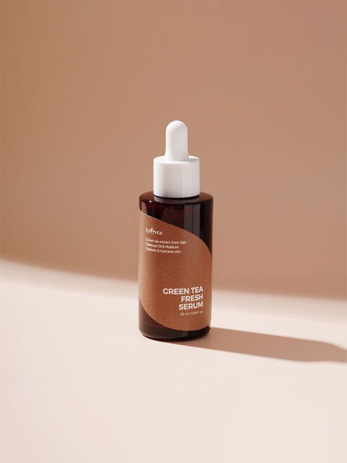 En liten brun flaske med pipettlokk, merket 'Green Tea Fresh Serum,' er vist på en beige bakgrunn.
