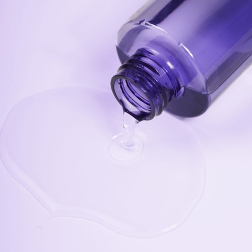 A purple bottle is pouring a clear liquid onto a white surface.