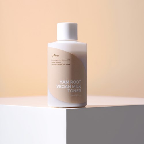 Eine weiße Flasche mit veganem Milch-Tonikum mit beiger Beschriftung, auf weißer Oberfläche vor hellem Hintergrund.