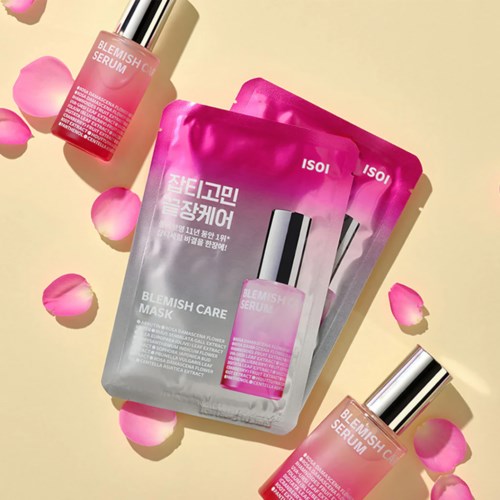 A skincare set with a pink and gray mask and two serum bottles, surrounded by pink rose petals.