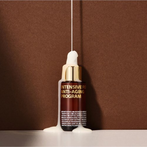 En liten flaske merket 'Intensive Anti-Aging Program' med et fall av hvit væske ved siden av.