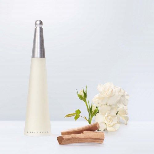 A white perfume bottle, white flowers, small green plant, and two wooden sticks on a white background.