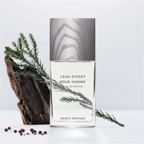 A perfume bottle with a sprig of pine, wood piece, and black peppercorns for decoration.