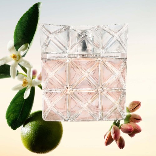 A square perfume bottle with a pinkish liquid, surrounded by leaves, flowers, and a citrus fruit.