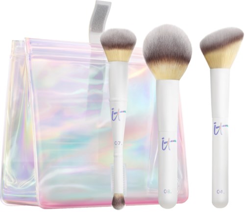 Four makeup brushes are placed in front of an iridescent storage bag. Brushes have white handles and fluffy bristles.