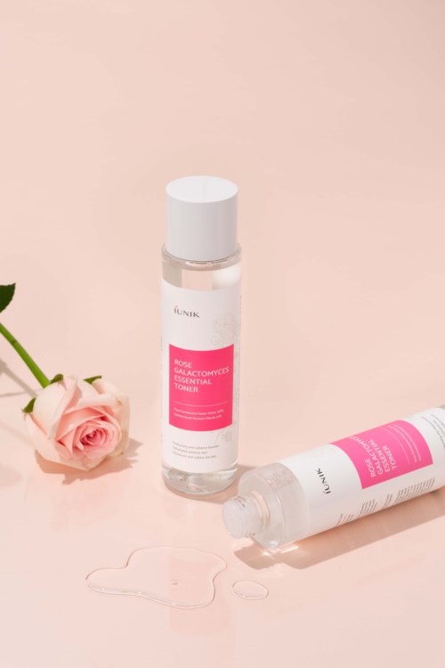 Två flaskor ansiktsvatten med rosa etiketter, en ligger ner och en står upp, bredvid en rosa ros.
