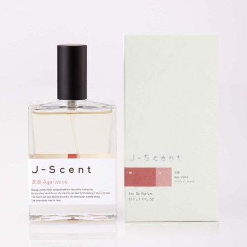 Eine klare Glasparfümflasche mit schwarzem Kapp und weißem Etikett, neben einer passenden weißen Box.