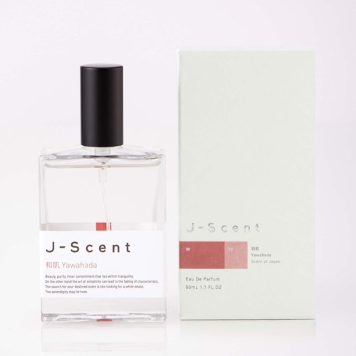 Ein transparentes Parfümflasche mit schwarzem Deckel und weißem Etikett neben einer weißen Box mit pinkem und schwarzem Text.