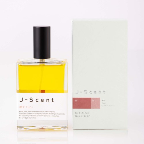 Ein Parfümflasche mit schwarzem Deckel und einer weißen Packung daneben, beide mit J-scent Beschriftung und gelber Flüssigkeit.