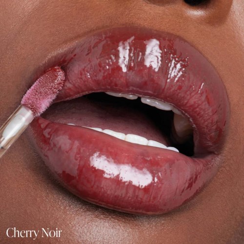 A person is applying pink gloss or lipstick to lips, which are slightly parted showing teeth.