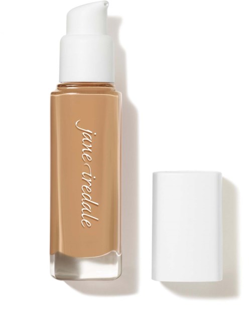 En beige flytande foundationflaska med vit lock och logga, placerad upprätt med lock borttaget.