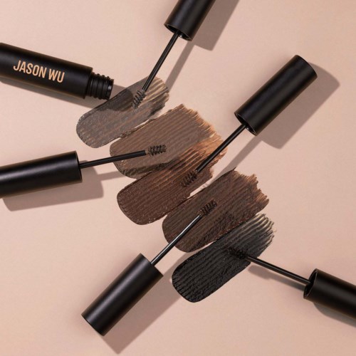 Drie zwarte mascara-tubes met borstels liggen op een beige achtergrond, elk geopend om verschillende tinten te tonen.