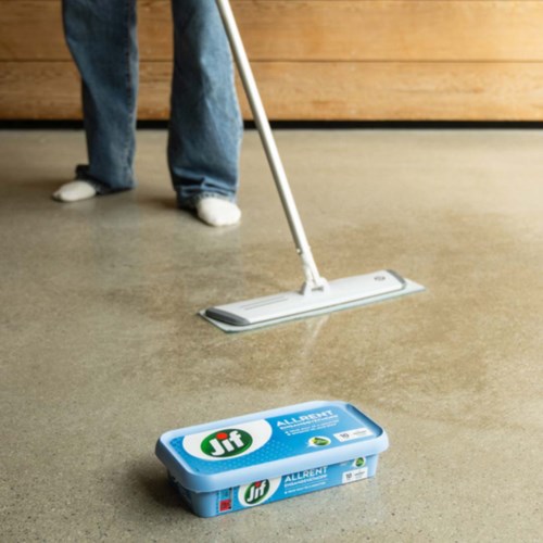 Person som mopper gulvet med en flat mop, iført jeans og hvite sko.