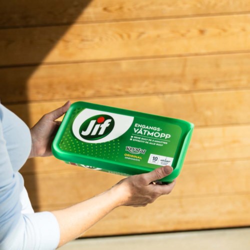 En person holder en grønn boks Jif margarin med treflis i bakgrunnen.