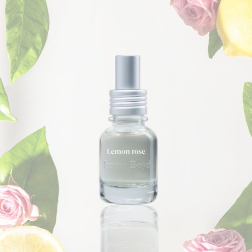Pieni lasipullo, jossa lukee Lemon Rose, spraykaulalla, ympärillä pinkkejä ruusuja ja sitruunoita.