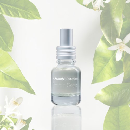 Pieni läpinäkyvä suihkepullo, jonka etikossa lukee 'Orange blossom', vihreiden lehtien ja valkoisten kukkien ympäröimänä.