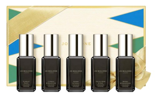 Five nail polish bottles in front of a decorative box with a gold, green, and blue geometric design.