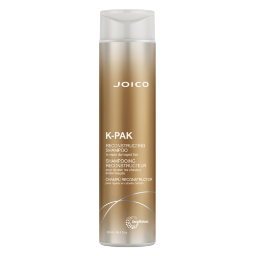 A tall, gold-colored bottle with a white cap, labeled 'JOICO K-PAK RECONSTRUCTING SHAMPOO.'