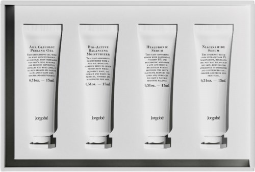 Four white tubes with black caps, labeled skincare products, are arranged in a row in a display case.