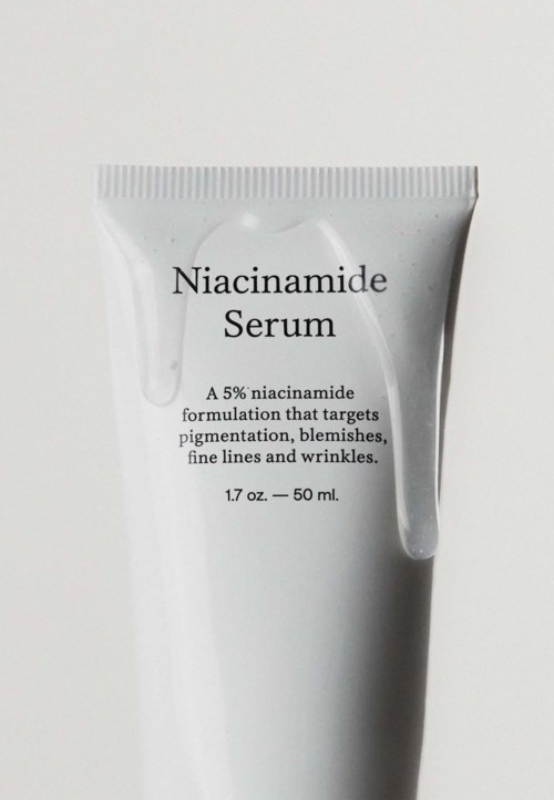 En vit tub för niacinamid serum, 50 ml, med svart text som beskriver dess syfte och ingredienser.