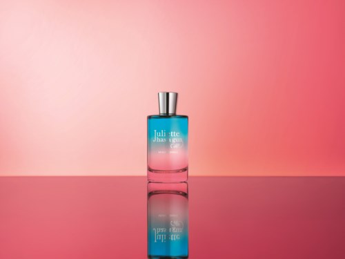 En parfyllflaska i blå och rosa gradient med silverlock, placerad på en reflekterande yta mot en rosa bakgrund.