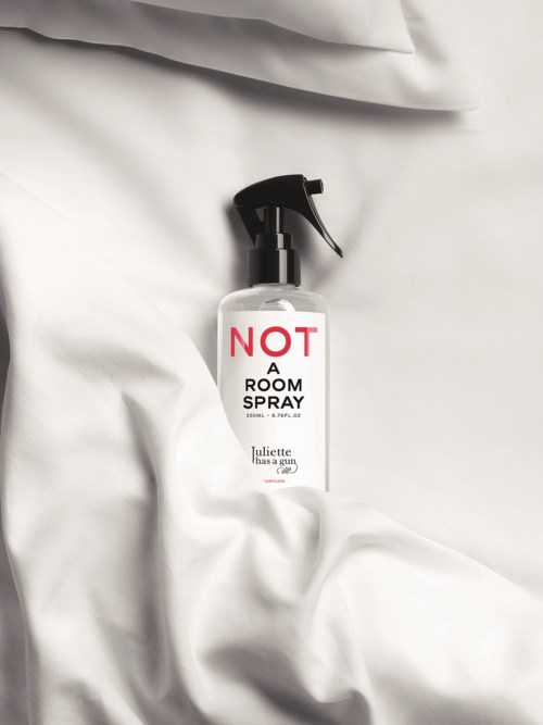 En sprayflaska med en etikett som säger "NOT A ROOM SPRAY" är placerad på vit tyg.