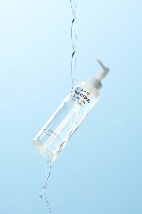 Eine klare Flasche mit Gesichtsreinigungsprodukt hängt, Wasser spritzt um sie.