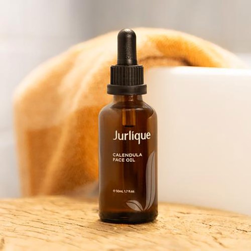 En liten brun flaske med Jurlique Calendula Face Oil med pipette, plassert på en treoverflate.