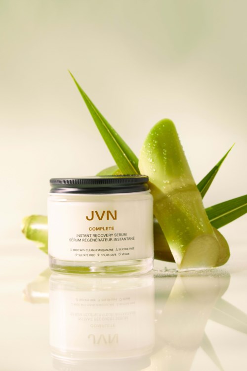 En burk av JVN Complete-serum med aloe vera blad och skivor i bakgrunden.