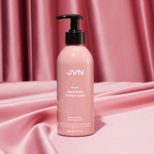 En rosa flaska JVN Revive Repairing Conditioner på rosa tyg, med ett svart pumplock.