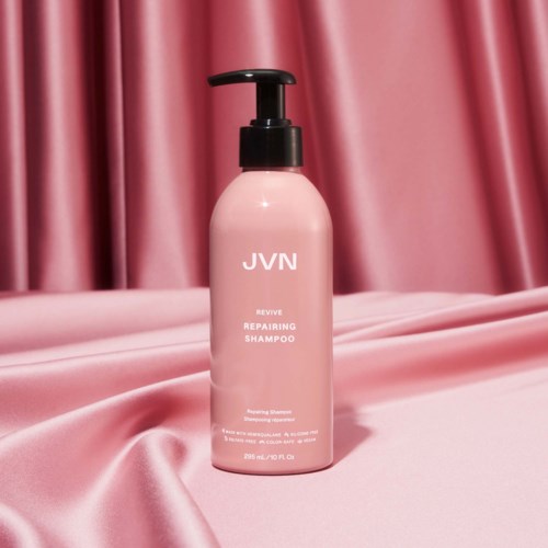 En rosa flaska med JVN reparationsschampo med svart pump, mot rosa satin gardiner och tyg.
