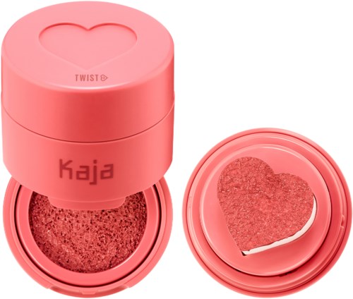 Rosa rund behållare med ett hjärtformat stämpel, innehåller sminksvamp eller rouge med hjärtform, och ett avtagbart lock.