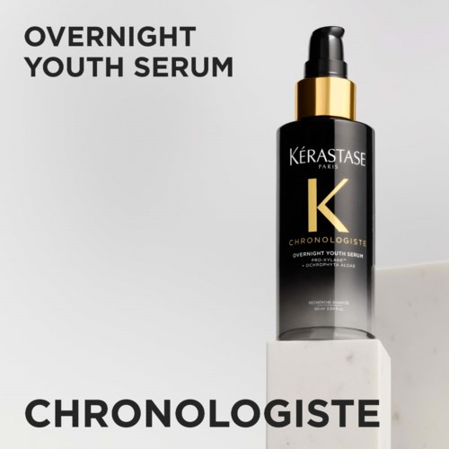 Eine schwarze Flasche mit Goldkappe und Pipette für Overnight Youth Serum von Kérastase, auf einem weißen Block.