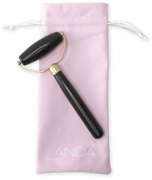 En svart ansiktsrulle med guldförsedd handtag på en rosa påse märkt 'ANDA'.