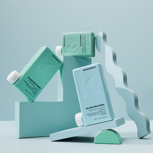 Kolme pulloa Kevin Murphy Killer Curls Wash -shampoita esillä minimalistisessa, modernissa taustassa sinisen ja valkoisen sävyissä.