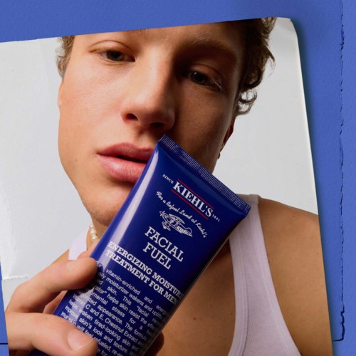 A young man holding a blue tube of facial moisturizer close to his face.