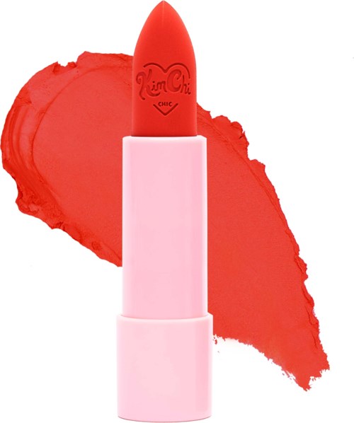 A pink lipstick with a red-orange tip, lying on a blurred lipstick smear. The brand name is on the lipstick. Bright colors.