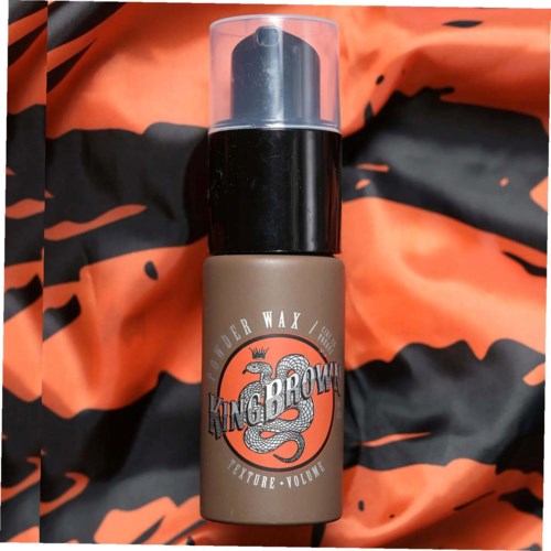 En flaske mærket 'King Brown' med en slangedesign, holdt mod en orange og sort stofbaggrund.