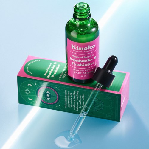 En grön flaska märkt 'Kinoko' och en pipett är placerade på en rosa och grön förpackning, möjligen hudvårdsprodukter.