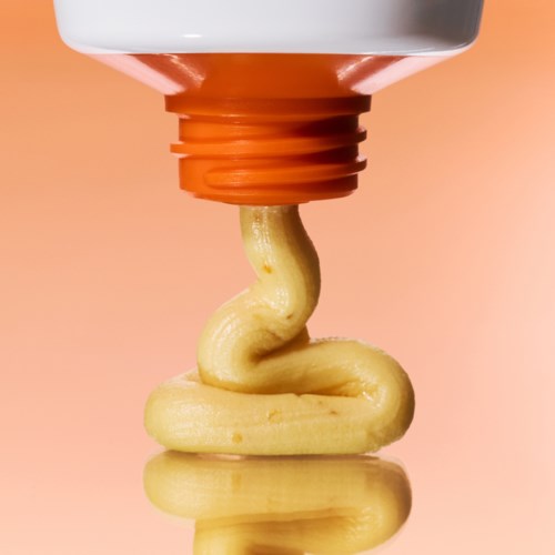 Cream is squeezed out of a tube, forming a swirl on a peach-colored background.