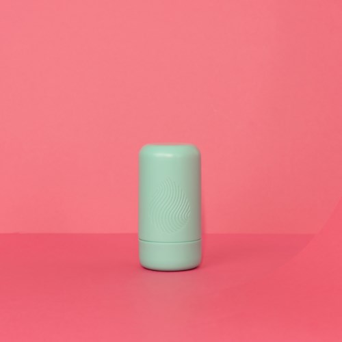 En pasta grønn sylinderformet gjenstand står på en rosa bakgrunn, med et subtilt mønster på overflaten.