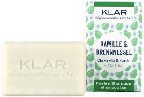 Sæbeplade med urtelugt ved siden af emballage med blade og blomster, mærket som shampoo bar og naturlige ingredienser.
