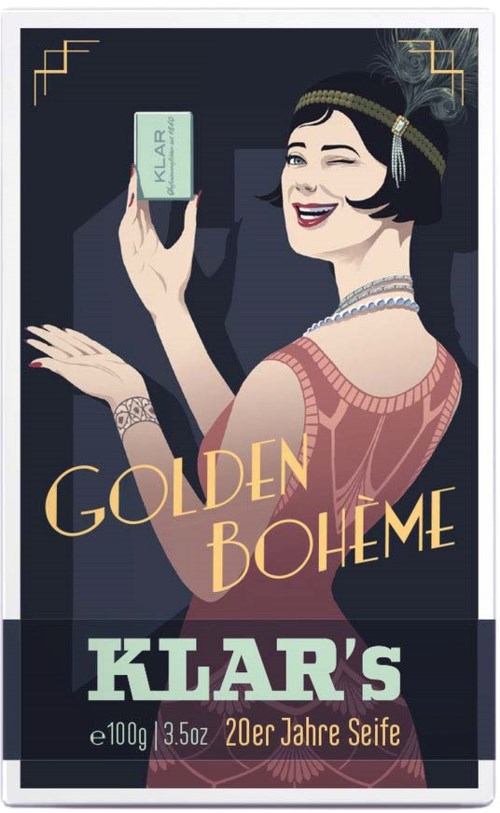 Kobieta w stylu lat 20. z biżuterią trzyma mydło, uśmiecha się. Etykieta mówi 'Klar' i 'Golden Boheme'.
