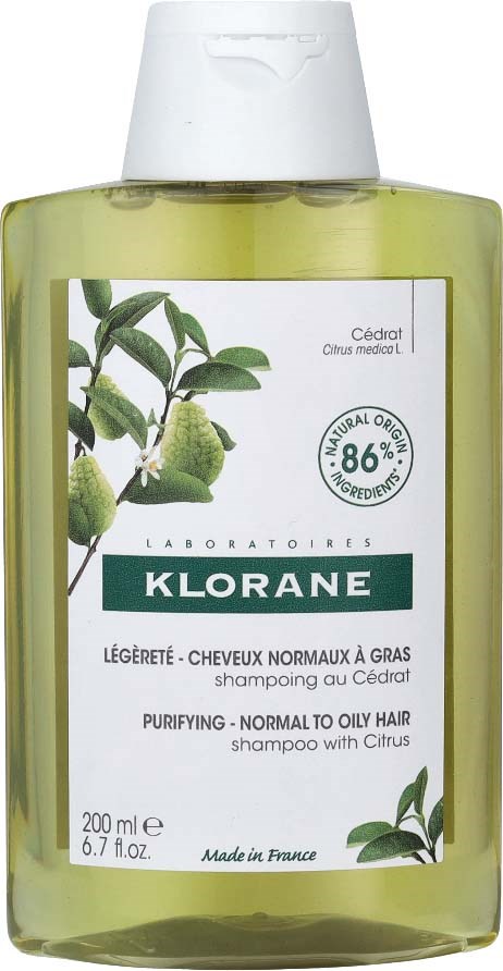 A clear yellow-green bottle of shampoo with a white cap, showing citrus fruit and green leaves on the label.