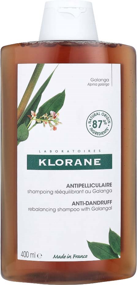 A brown bottle with a white label, green leaves, and small white flowers, containing anti-dandruff shampoo with natural ingredients.