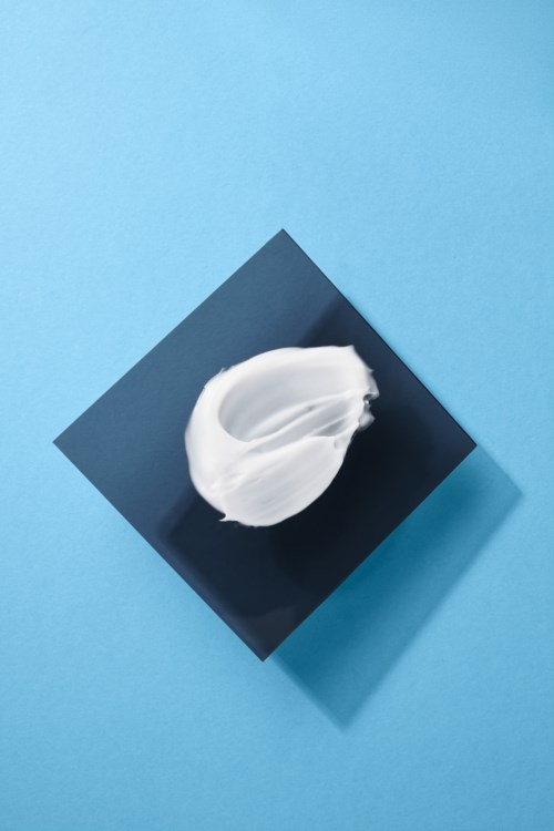 Weiße Creme auf einem schwarzen Quadrat vor einem hellblauen Hintergrund, mit Schatten für Tiefe.
